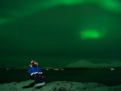 Gjester sitter ved fjorden og skikker på nordlyset