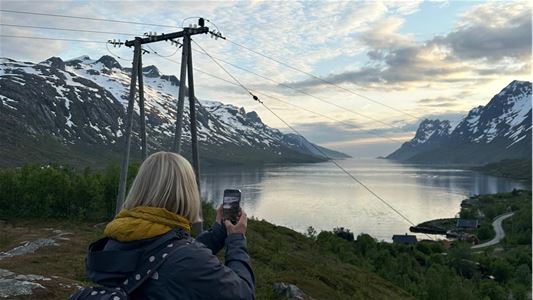 A person taking  a picture of the fjord and mountains
