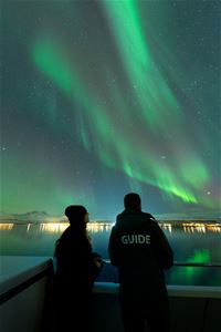 Two people viewing the Northern Lights from the boat's deck