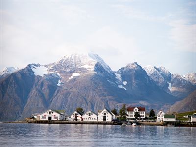 Utsikt over liten bygd på en øy foran fjellene og ved fjorden