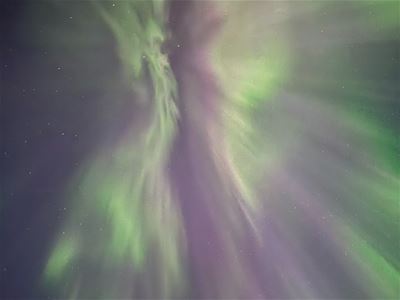 Green and purple Northern Lights form a corona high in the Arctic night sky.