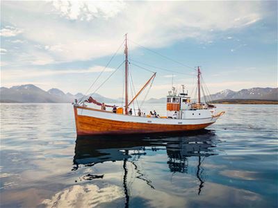 The historic wooden vessel Hermes II, built in 1917, sailing through Tromsø Sound, surrounded by mountains and beautiful Arctic coastal scenery.