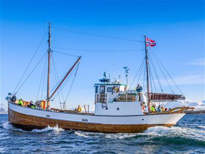 The traditional wooden vessel Hermes II cruising through the Arctic coastal waters near Tromsø on a scenic sightseeing and photography tour.