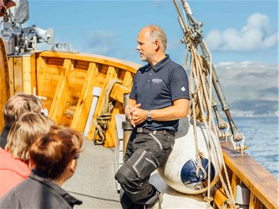 A guide sharing stories about Hermes II and Tromsø's maritime history with guests during a sightseeing cruise through Tromsø Sound.