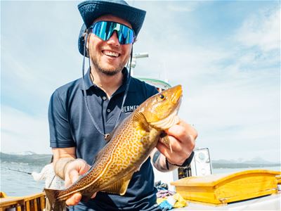 A smiling guide holding a freshly caught fish aboard Hermes II during a guided fishing and fjord cruise from Tromsø.