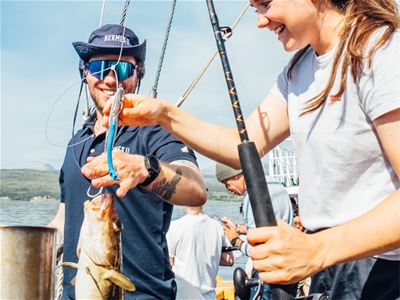 A guide helping a guest with their catch aboard Hermes II during a guided fishing cruise along the Arctic coast near Tromsø.