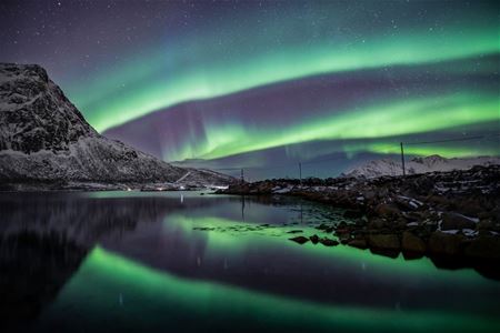 Green Northern Lights above a quiet fjord and snow-covered mountains in Northern Norway, reflected in the water.