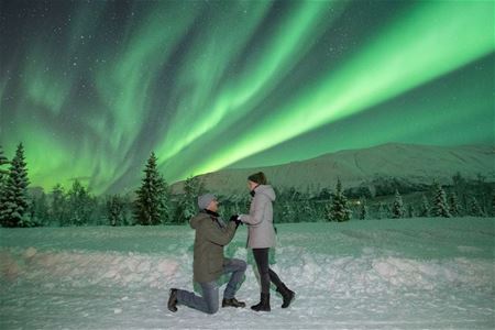 A guest proposing to their partner beneath green Northern Lights in a snowy Arctic landscape.