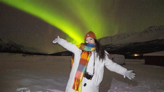 En gjest står under nordlyset i det snødekte arktiske landskapet under en nordlysopplevelse.