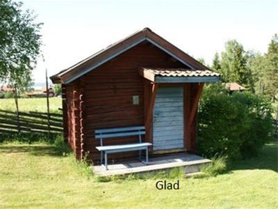 Stuga Glad är en röd liten timmerstuga med blå dörr och en blå bänk bredvid dörren. 