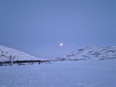 Snødekte fjell og et åpent vinterlandskap under en lys himmel i blå og rosa nyanser.