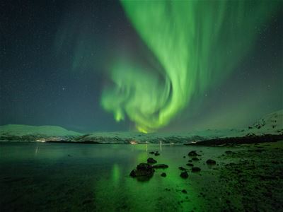 Nordlys som speiler seg i fjorden med snødekte fjell i bakgrunnen