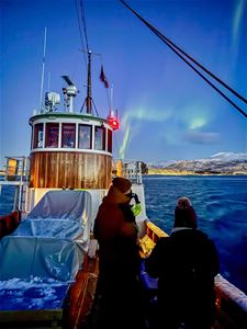 Gjester nyter den arktiske kvelden fra dekket på Hermes II, med nordlyset synlig over fjellene ved Tromsø.