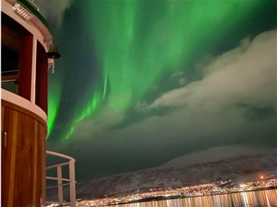Grønt nordlys lyser opp himmelen over Tromsø, sett fra dekket på den historiske trebåten Hermes II.