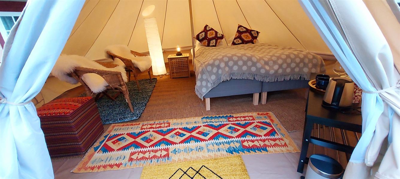 Interior of a glamping tent with a bed, rugs, and a small seating area, decorated with warm colors and textiles.