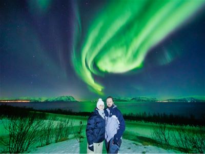 Et par poserer sammen under grønt nordlys i vinterlandskapet.
