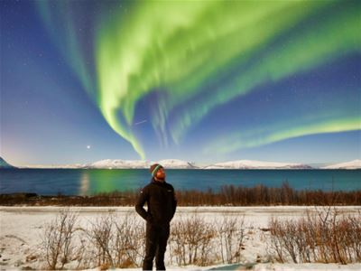 En gjest ser opp på nordlyset over det snødekte landskapet.