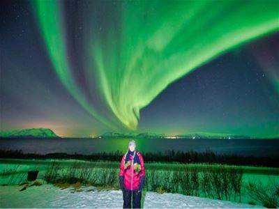 En gjest står under kraftig grønt nordlys på nattehimmelen.