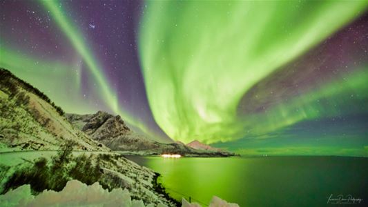 Green Northern Lights reflect in the water surrounded by mountains and winter landscape.