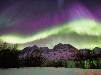 Green and purple Northern Lights above snow-covered mountains and winter scenery.