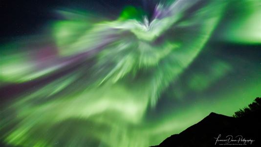 Intense green Northern Lights dance above the mountains at night.