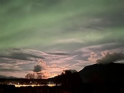 Northern lights above fjords and mountains during an Arctic evening near Tromsø.