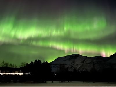 Grønt nordlys over fjellandskapet utenfor Tromsø på tur med Aurora Exclusive