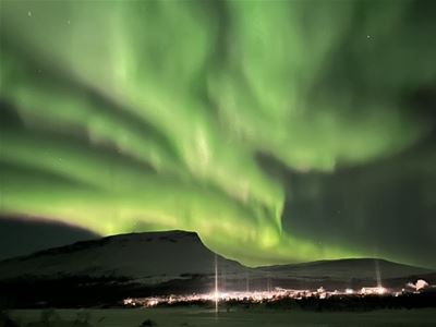 Kraftig grønt nordlys over fjell og lysene fra bebyggelsen i Tromsøregionen.