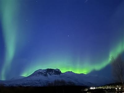 Grønt nordlys over et snødekt fjellandskap i Tromsøregionen på tur med Aurora Exclusive.