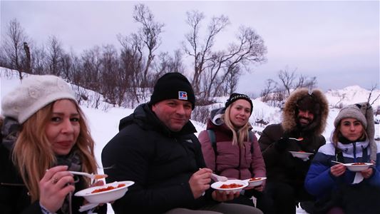 Guests enjoy a food break by the campfire during a private snowshoe trip on Kvaløya.