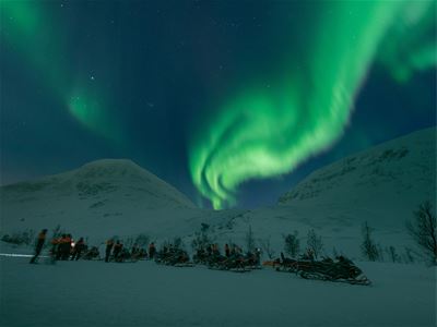 Snowmobiles stand ready, while the Northern Lights appear overhead