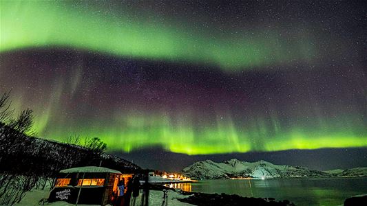 Grønt nordlys lyser over det arktiske landskapet og fjellene.