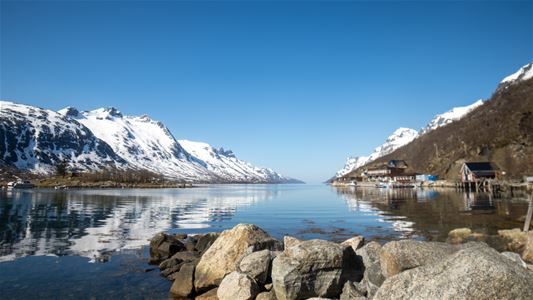 A calm fjord surrounded by snow-covered mountains and coastal scenery in Northern Norway.