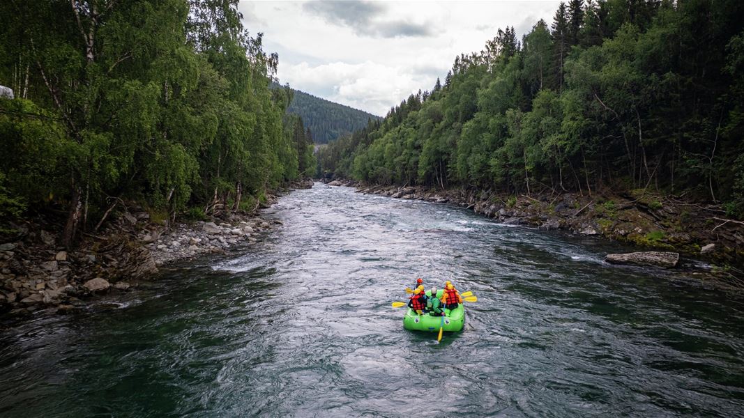 Raftingflåte midt i strømmen på Sjoa-elva, med skogkledde dalsider på begge sider.
