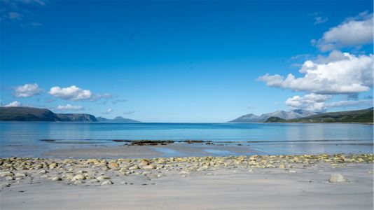 Hvit sandstrand med utsikt mot havet og fjellene på Vannøya