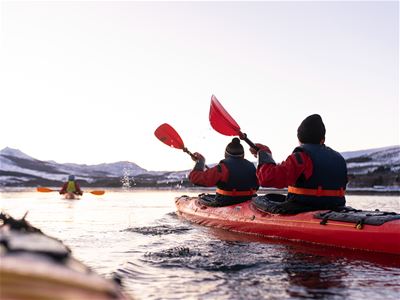 Gjester padler kajakk på fjorden ved Sommarøy, omgitt av fjell og arktisk kystlandskap.