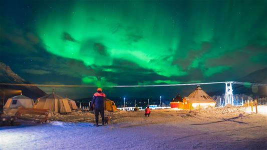 Kraftig nordlys over Tromsø Laplands reinsdyrleir og lavvoer i snødekt landskap.