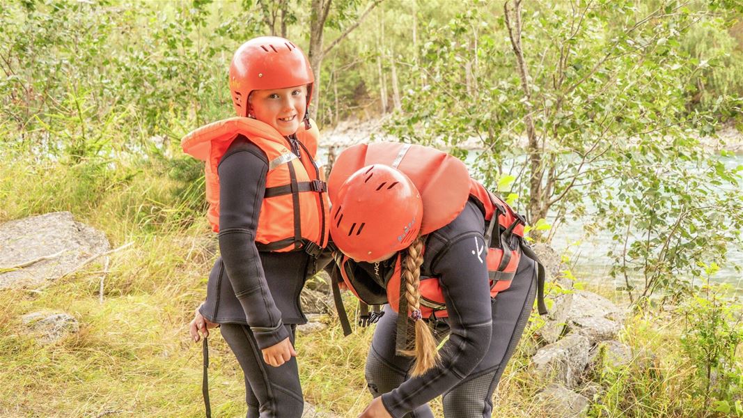 Deltakere med raftingutstyr ved elvebredden.