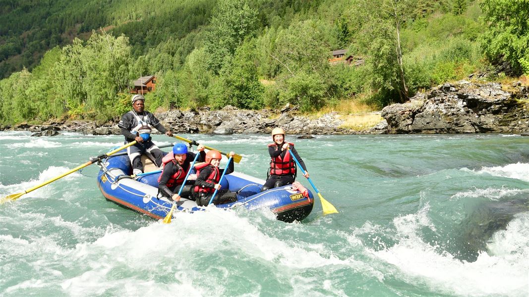 Raftingbåt på strykende elv omgitt av fjell og skog.