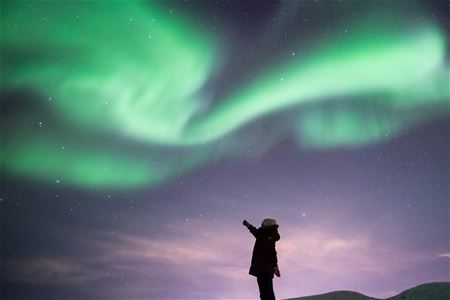 Gjest som peker mot nordlyset i det snødekte landskapet