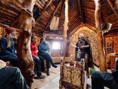 Gjester lytter til historier om vikingliv og kultur inne i en av bygningene i vikinglandsbyen.