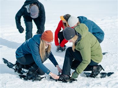 Visitors prepare their snowshoes in a snowy Arctic landscape during a guided hiking experience to a hidden Viking village near Tromsø.