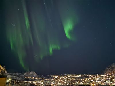 Green Northern Lights dance across the night sky above the lights of Tromsø.