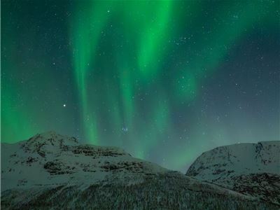 Green Northern Lights stretch across the night sky above snow-covered mountains in Northern Norway. A beautiful example of what guests may experience on a guided Northern Lights chase from Tromsø.
