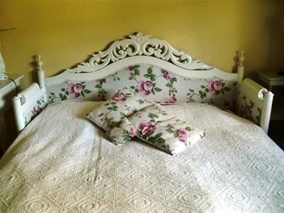 Säng med vitt överkast och en sänggavel av en vitmålad kökssoffa med blommig stoppning. 