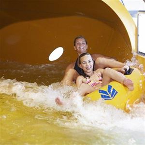 Två tjejer sitter i en gummibåt och de åker i vattenrutschbana. 