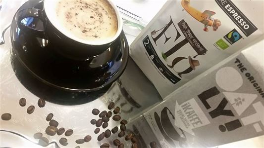 En svart kopp med skummar kaffe, kaffebönor på bordet, en förpackning med kaffe och en förpackning med Oatley  I kaffe.
