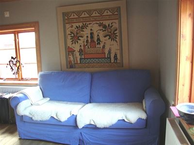 Blå tvåsitssoffa med vita fårfällar i soffan och en tavla på ålderstrappan ovanför soffan. 