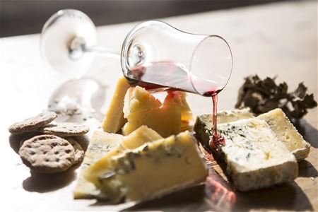 Various cheeses placed on a dish with biscuits and a glass of wine.