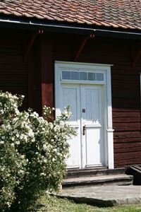 Ett hus med vita pardörrar med en stor rosbuske intill ingången. 